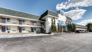 A motel with a 'Welcome' sign, parking spaces, and a clear sky.