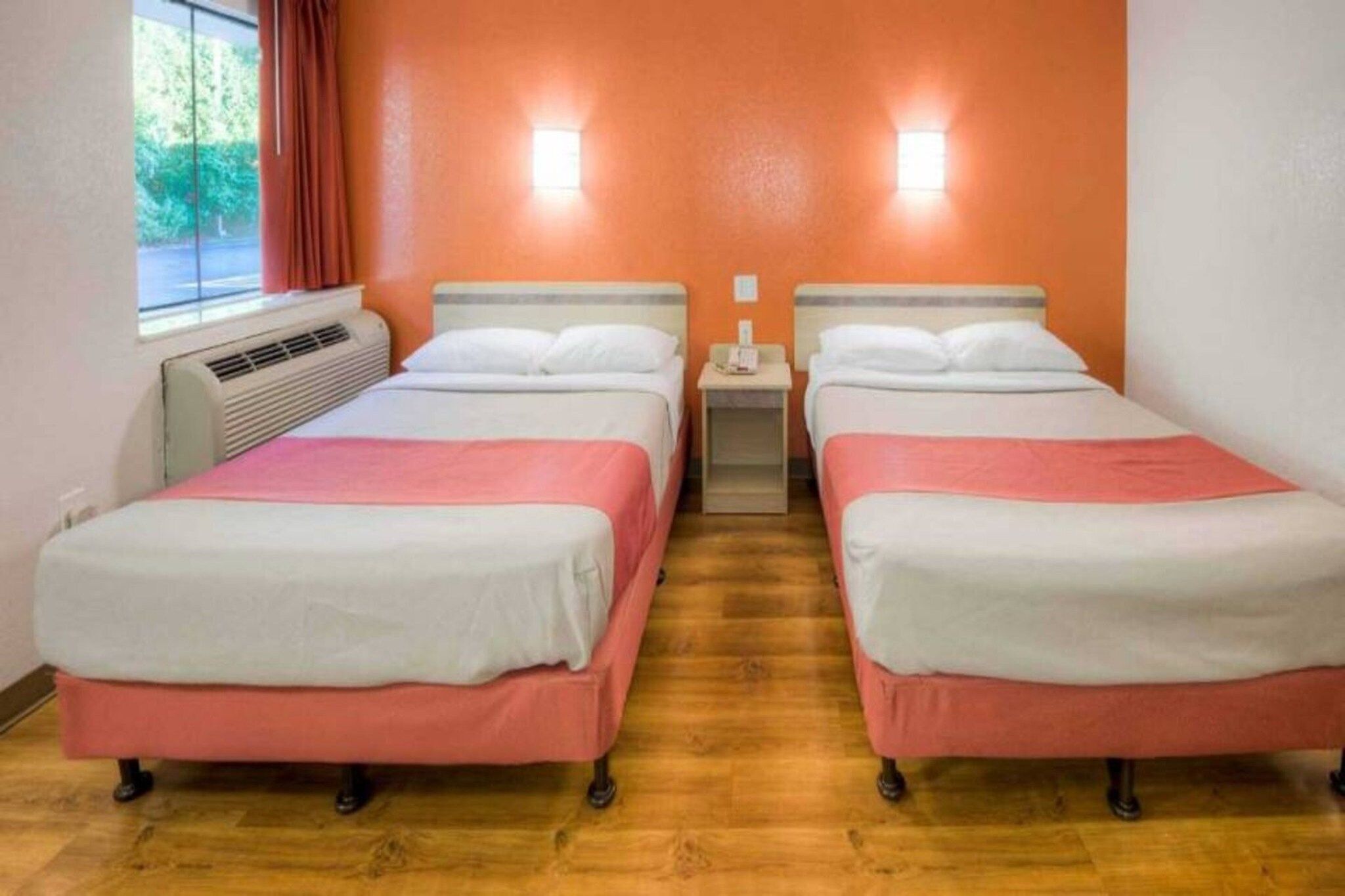 Una habitación con dos camas, una ventana con cortinas, un equipo de aire acondicionado y una mesita de noche con un teléfono.