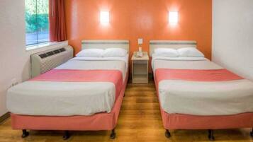Una habitación con dos camas, una ventana con cortinas, un equipo de aire acondicionado y una mesita de noche con un teléfono.