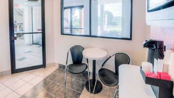 Un hall de hotel con puerta de vidrio, una pequeña mesa redonda con sillas y un basurero con útiles de limpieza.