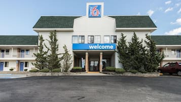 Un motel con un letrero que dice 'Welcome', un estacionamiento y un coche rojo aparcado fuera.