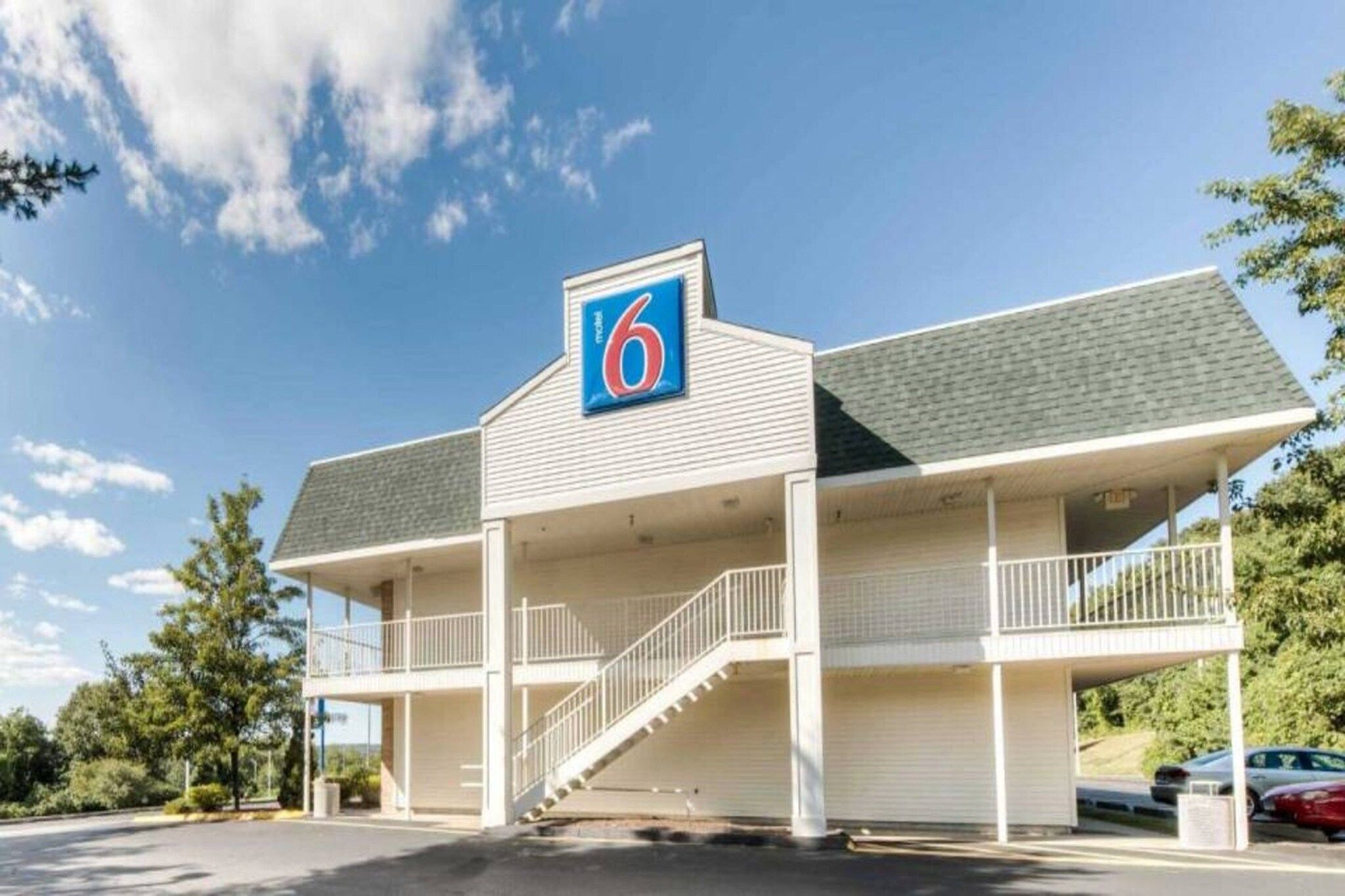 Un motel con un llamativo letrero con el número '6', una zona de estacionamiento techada y una escalera que conduce a la entrada.