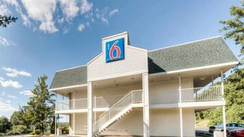Un motel con un llamativo letrero con el número '6', una zona de estacionamiento techada y una escalera que conduce a la entrada.