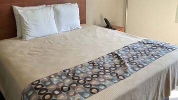 Ein Hotelzimmer mit einem Bett, Kissen, einer gemusterten Decke, einem Nachttisch mit Lampe und einem an der Wand befestigten Telefon.