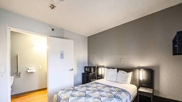 A hotel room with a bed, bedside tables, a microwave, and a door leading to a bathroom.
