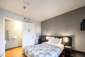 A hotel room with a bed, bedside tables, a microwave, and a door leading to a bathroom. - 1 Queen Bed | ADA/RI Shower/Micfridge (Wethersfield)