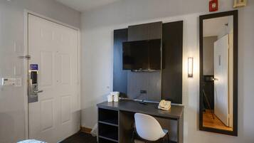 A hotel room with a bed, a desk with a chair, a flat-screen TV, a mirror, and a door with a lock.