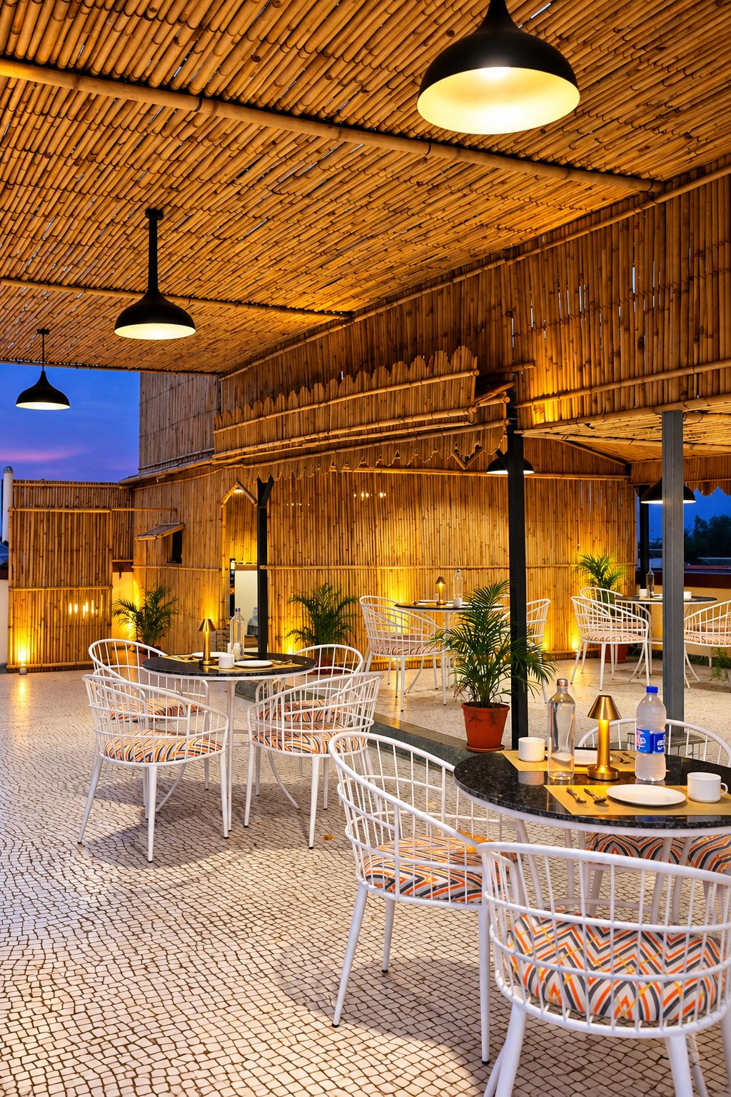 Un espace extérieur aménagé avec des chaises et des tables en métal blanc, un plafond en bambou et des plantes en pot.