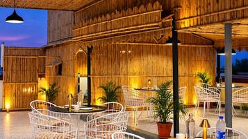 Un espace extérieur aménagé avec des chaises et des tables en métal blanc, un plafond en bambou et des plantes en pot.