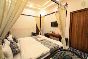 A four-poster bed with a canopy, a bedside table with a flat-screen TV, and a wooden door.