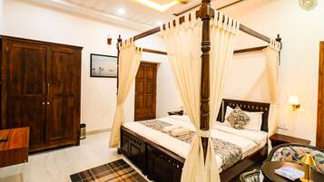 A four-poster canopy bed with a wooden frame and white curtains, a wooden wardrobe, a small bedside table with a lamp, and a patterned rug.