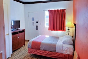 A hotel room with a bed, a desk, a television, a window with curtains, and a lamp.