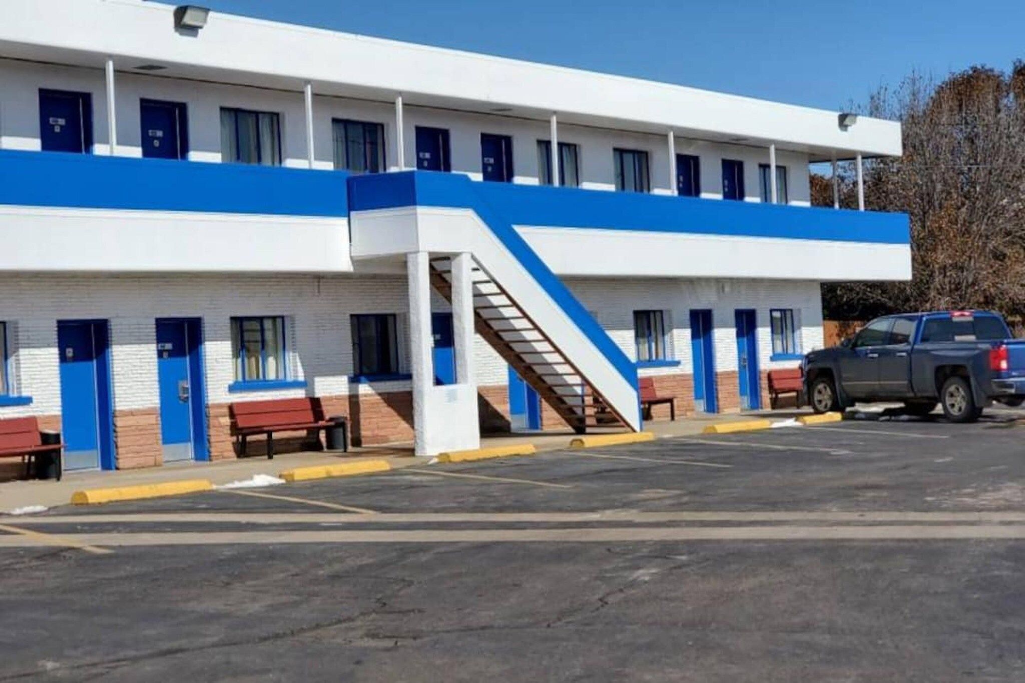 Un motel con una escalera central, varias habitaciones y un estacionamiento.