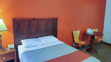 Una habitación de hotel con una cama, una mesita de noche, una lámpara, una silla y una pequeña mesa.