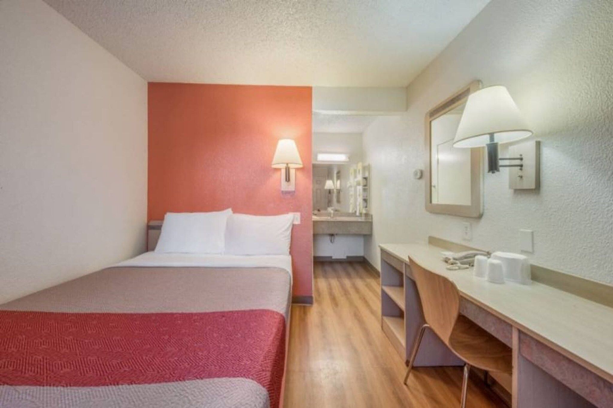 Een hotelkamer met een bed, een bureau, een spiegel en een badkamer in de achtergrond.