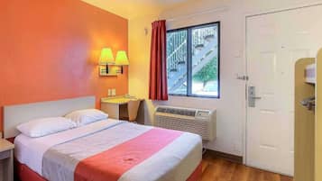 Habitación de hotel con cama, mesita de noche, lámpara, ventana y puerta.