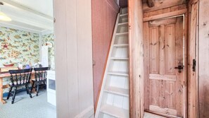 A wooden staircase leading to a door, a dining area with a table and chairs, and a wall with a patterned wallpaper.