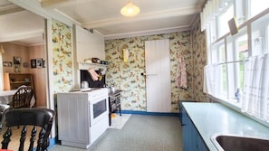 A compact kitchen with a stove, sink, and a window with curtains.