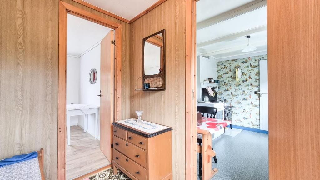 Habitación con armario de madera, espejo, cómoda y una zona de cocina con salpicadero estampado.