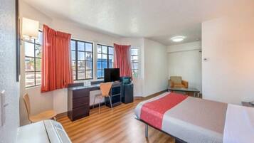 A hotel room with a bed, desk, chair, and a television.