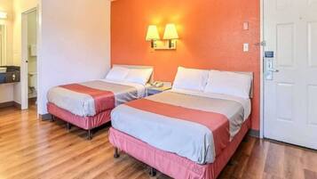 Une chambre d’hôtel avec deux lits, un plancher en bois, une porte blanche et une lampe fixée au mur.