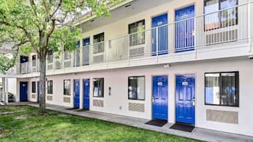 A two-story building with blue doors numbered 241 to 242, a balcony on the upper floor, and a tree in the foreground.