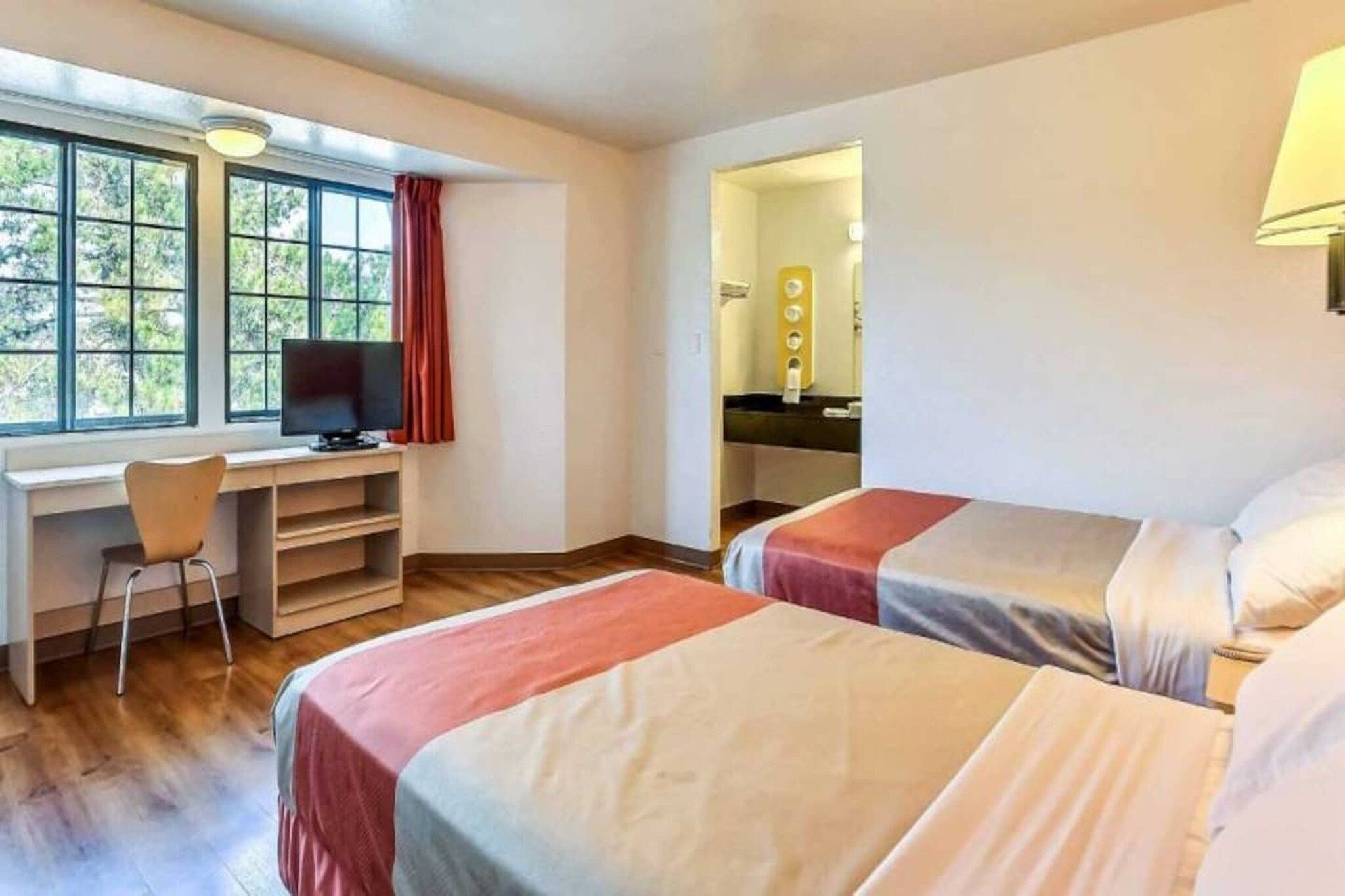 A room with two beds, a desk with a chair, a television, and a window with curtains.