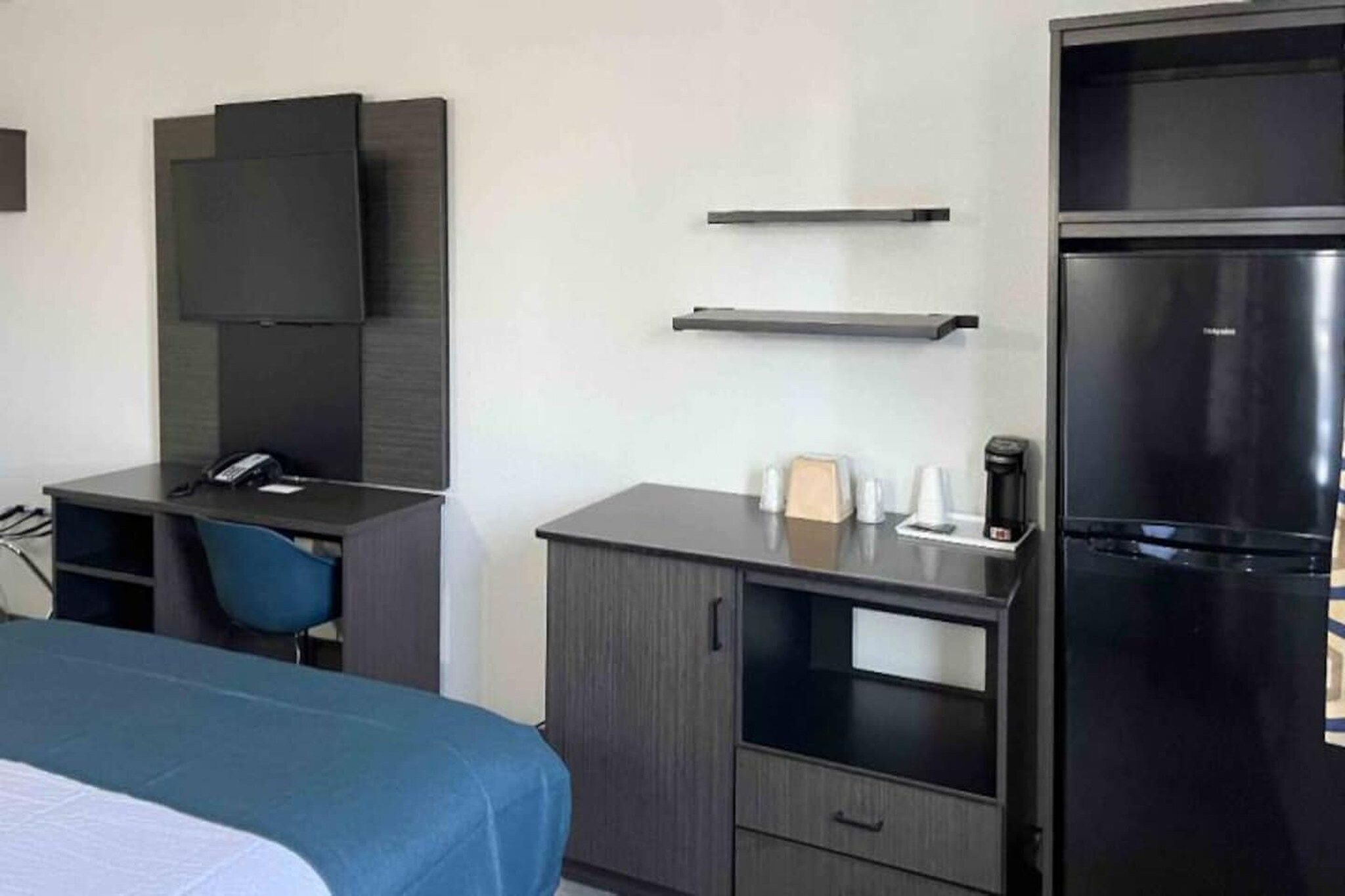 A hotel room with a bed, a desk, a chair, a flat-screen TV, a refrigerator, and a coffee maker.