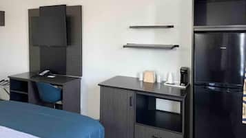 A hotel room with a bed, a desk, a chair, a flat-screen TV, a refrigerator, and a coffee maker.