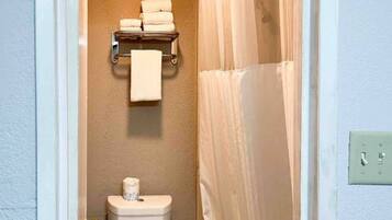 A bathroom with a toilet, a towel rack with folded towels, and a shower curtain.