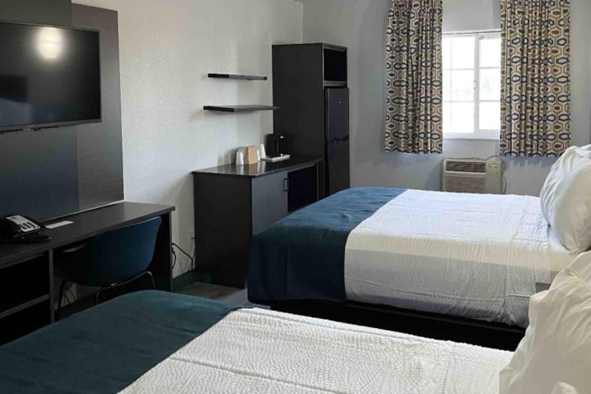 Ein Hotelzimmer mit zwei Betten, einem Schreibtisch, einem Fernseher, einem Kleiderschrank und einem Vorhang mit Muster.