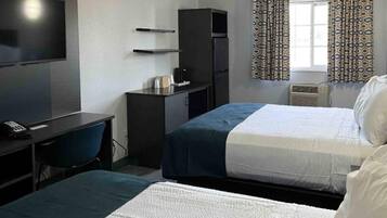 A hotel room with two beds, a desk, a TV, a wardrobe, and patterned curtains.