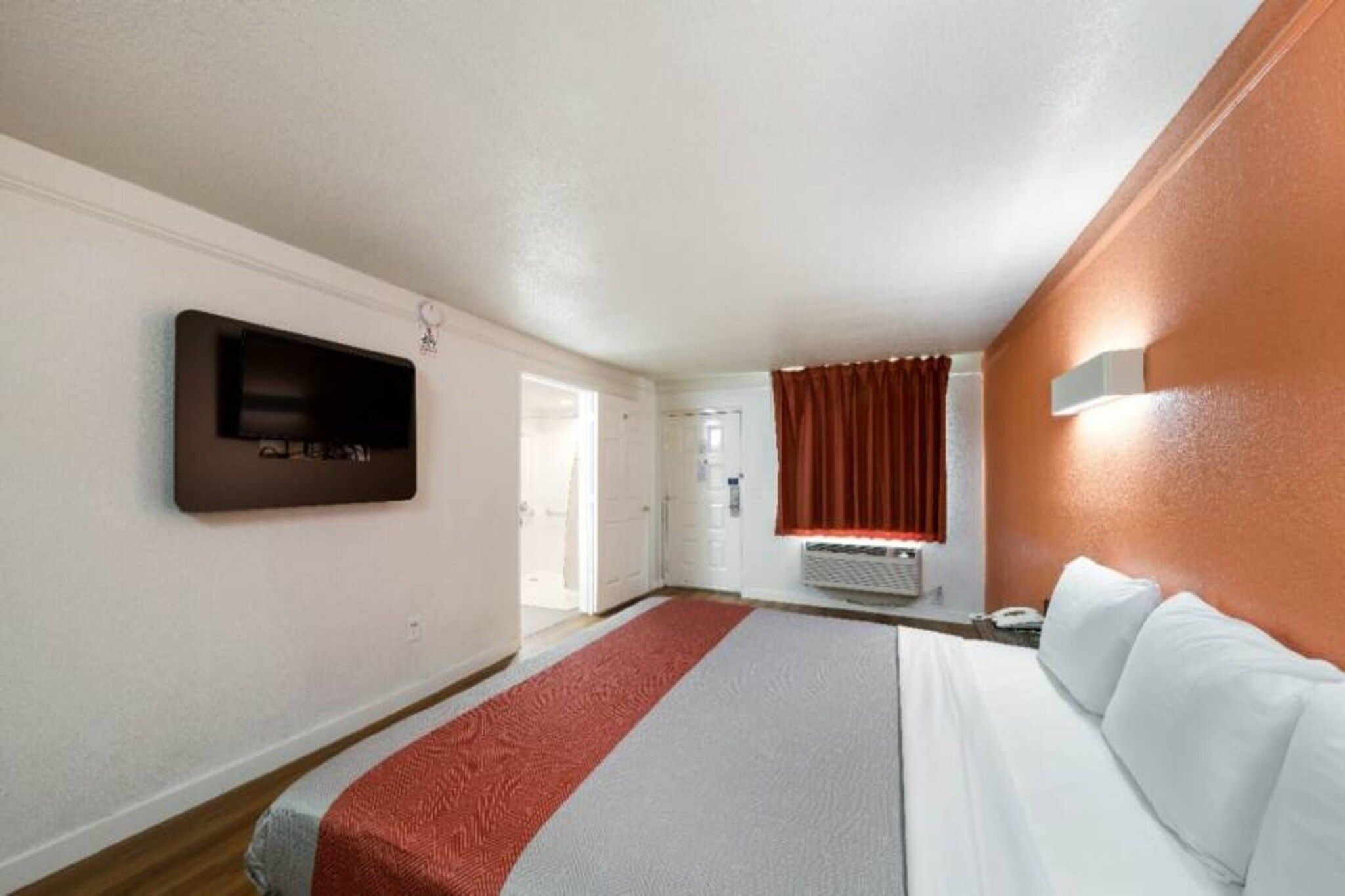 Ein Hotelzimmer mit einem Bett, einem kleinen Fernseher, einem Fenster mit Vorhängen und einer Tür.
