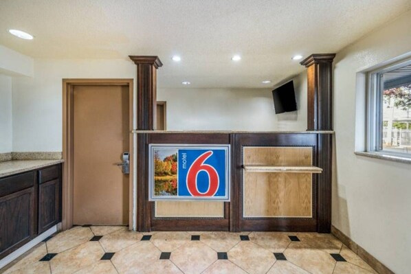 A hotel reception area with a large number '6' sign, a wooden reception desk, a door, and a window with a view.