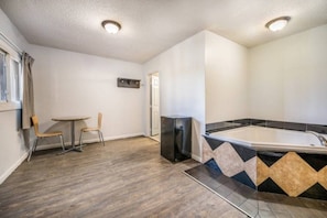 Ein Zimmer mit Holzboden, einem kleinen Tisch mit zwei Stühlen, einem schwarzen Kühlschrank und einem gefliesten Duschbereich.