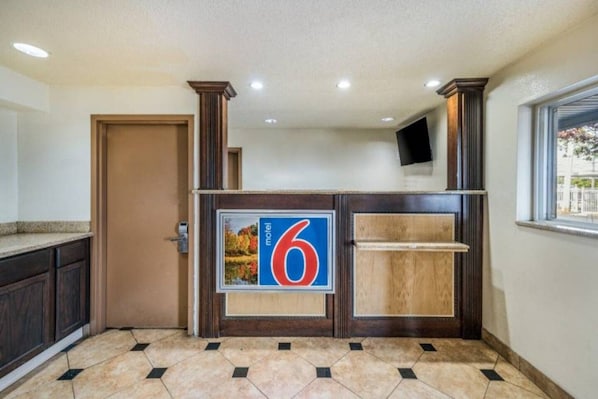 A hotel reception area with a large number '6' sign, a wooden reception desk, a door, and a window with a view.