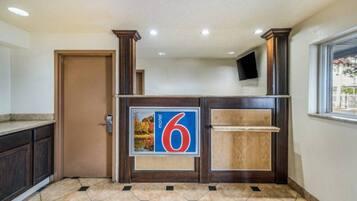 Een hotel receptie met een groot bord met het nummer 6, een houten receptiebalie, een deur en een raam met uitzicht.