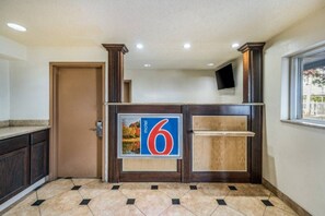 A hotel reception area with a large number '6' sign, a wooden reception desk, a door, and a window with a view. - 2 Full Beds | ADA/RI Shower/Mini Fridge (Rancho Mirage)