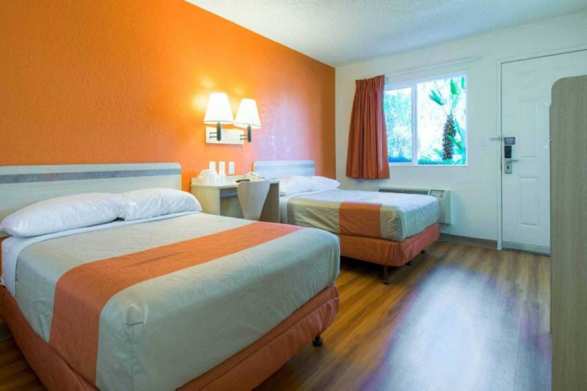 Ein Hotelzimmer mit zwei Betten, einem Nachttisch, einer Lampe, einem Fenster mit Vorhängen und einer Tür.