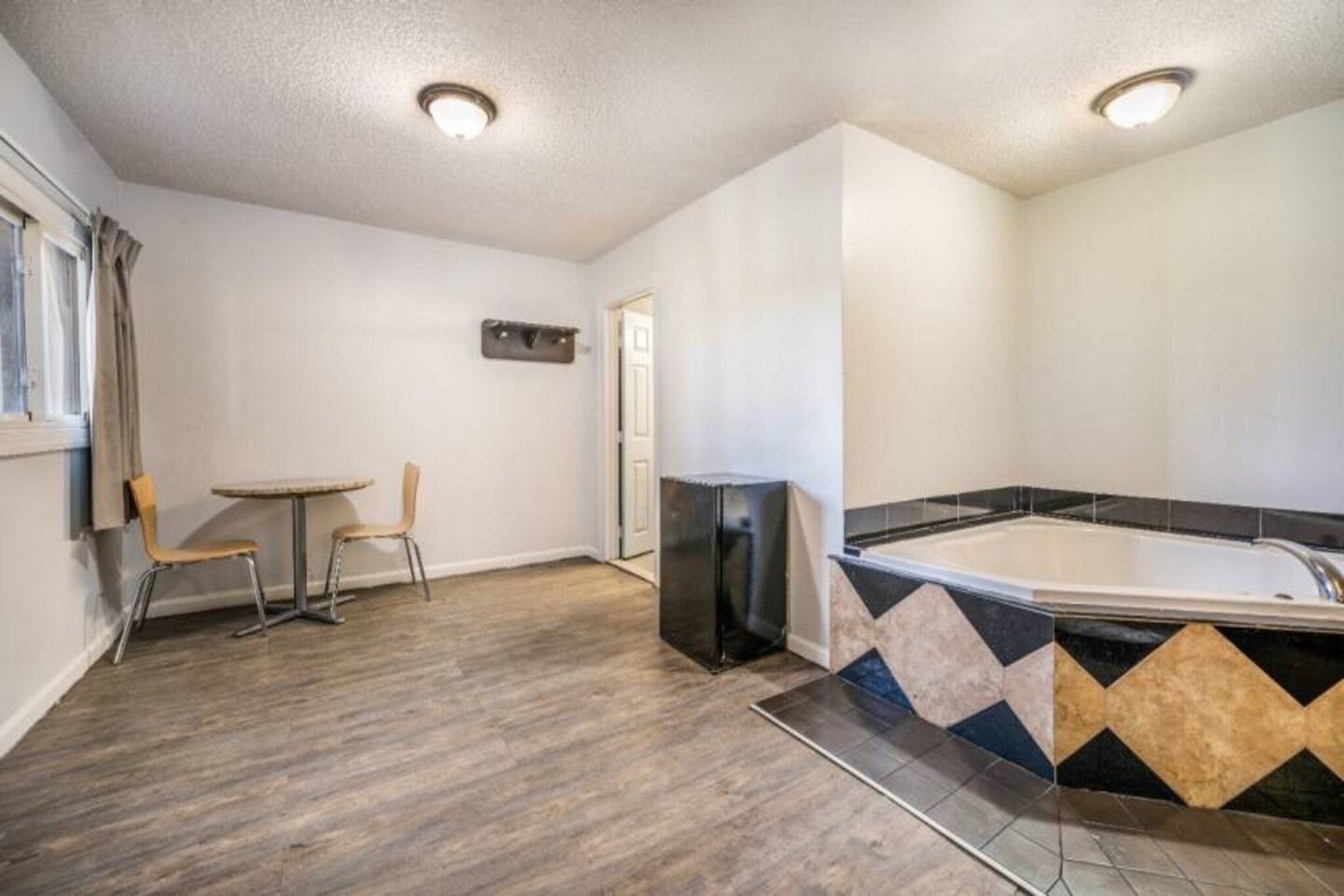 Ein Zimmer mit Holzboden, einem kleinen Tisch mit zwei Stühlen, einem schwarzen Kühlschrank und einem gefliesten Duschbereich.