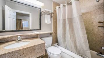 Baño con lavamanos de encimera de granito, inodoro blanco, ducha con cortina blanca y espejo con toallero.