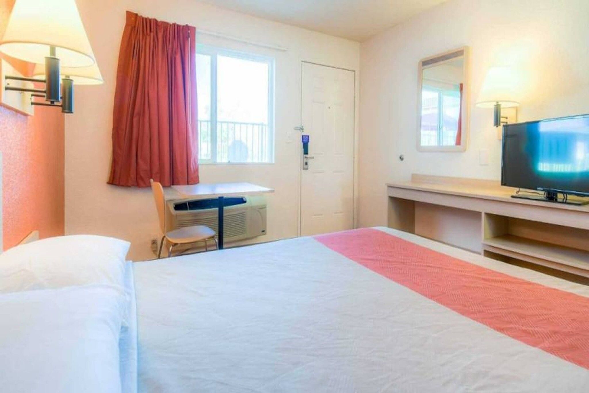 Una habitación de hotel con cama, escritorio, silla, televisor y ventana con cortinas.