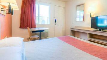 Una habitación de hotel con cama, escritorio, silla, televisor y ventana con cortinas.