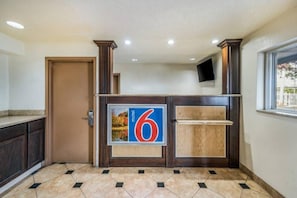 Zona de recepción de un hotel con un letrero grande con el número 6, un mostrador de madera, una puerta y un suelo de baldosas.