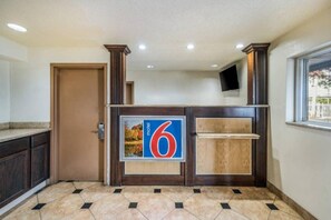 Ein Hotel-Empfangsbereich mit einem großen Schild mit der Zahl 6, einem hölzernen Empfangstresen, einer Tür und einem gefliesten Boden.