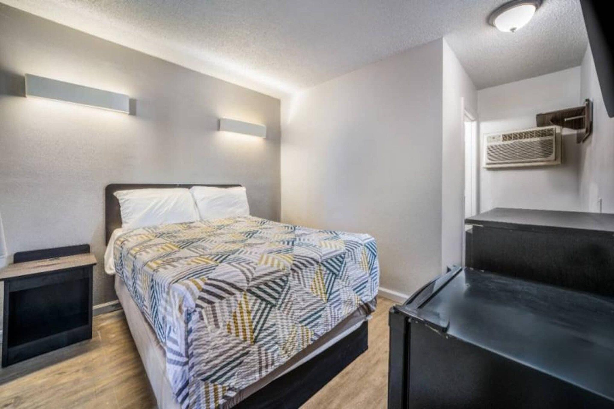 Een slaapkamer met een bed, nachtkastjes, een kaptafel en een wandgemonteerde airconditioning.