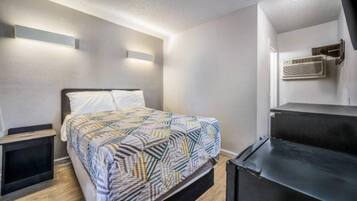 Een slaapkamer met een bed, nachtkastjes, een kaptafel en een wandgemonteerde airconditioning.