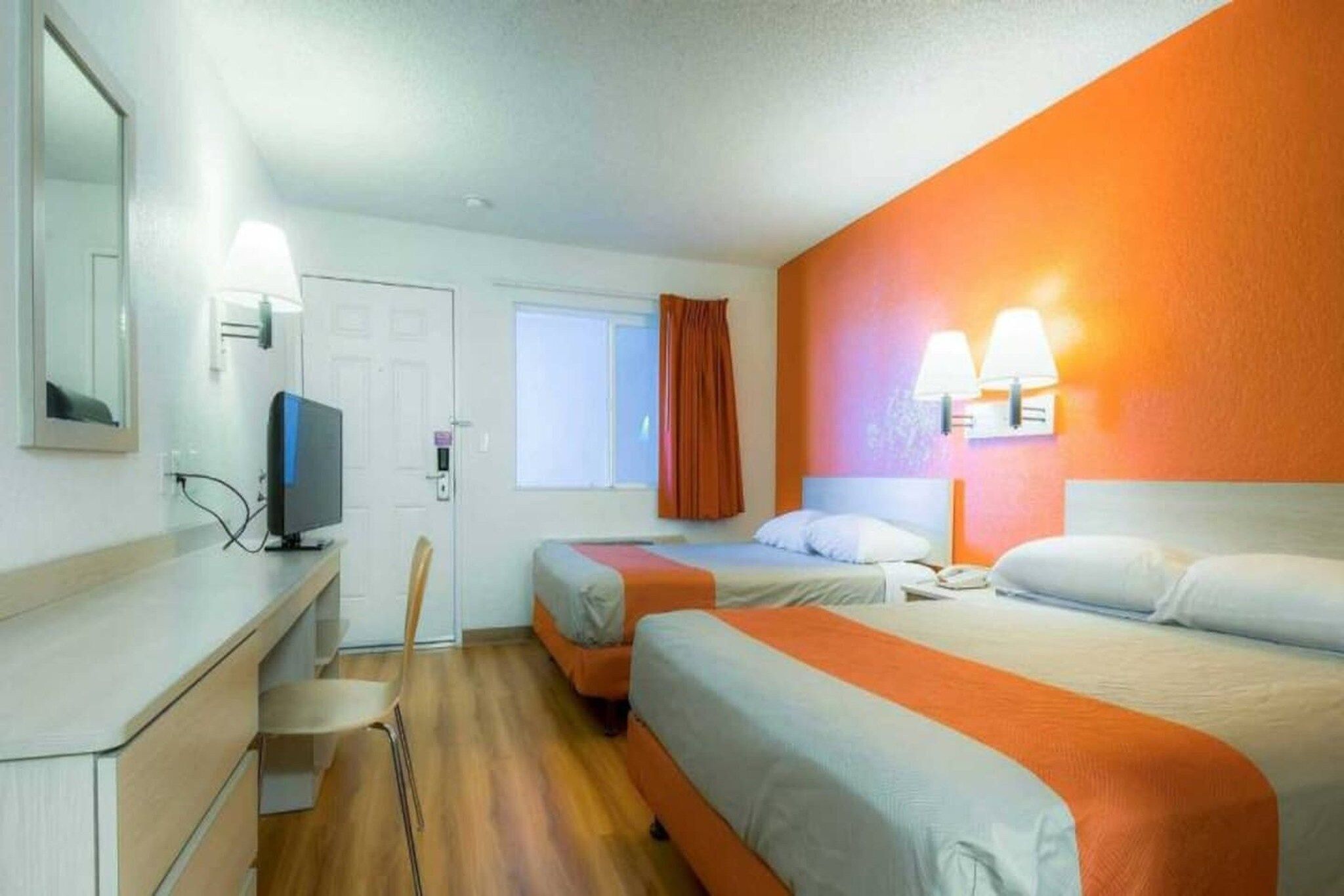 Ein Hotelzimmer mit zwei Betten, einem Schreibtisch, einem Sessel, einem Fernseher und einem Fenster mit Vorhängen.