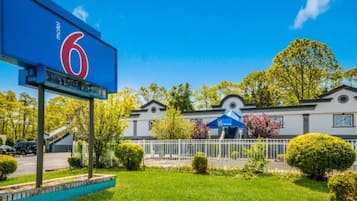 Un motel reconnaissable à son grand panneau indiquant le chiffre « 6 », doté d’un parking clôturé et d’un bâtiment à l’architecture moderne.