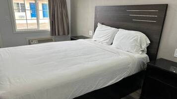Quarto de hotel com cama, mesa de cabeceira, janela com cortinas e luminária na parede.